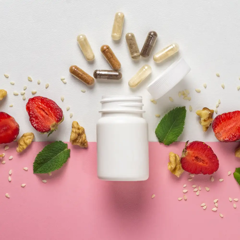 Compléments alimentaires en gélules disposés autour d’un flacon blanc, accompagnés de fraises, noix, graines de sésame et feuilles de menthe sur fond rose et blanc.